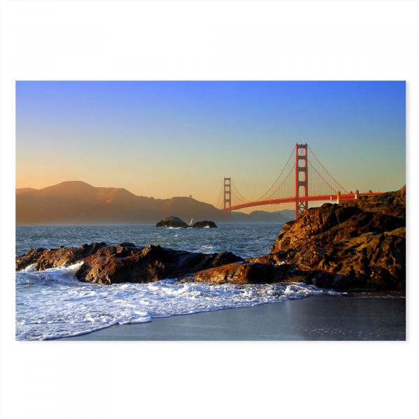 Golden Gate Bridge bei Sonnenuntergang, Wellen brechen an Felsen, im Hintergrund San Francisco Bay.