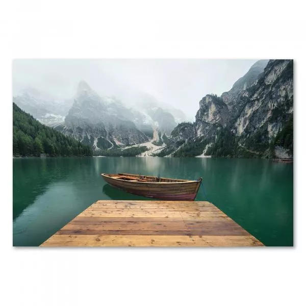 Holzsteg führt auf Bergsee, majestätische Berge im Nebel, einsames Boot.