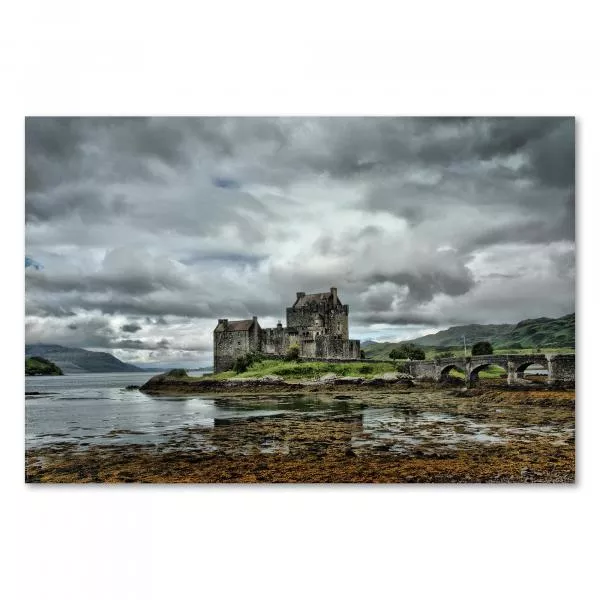 Spiegelbild von Eilean Donan Castle im Wasser und Steinstränden, drohender Himmel im Hintergrund.