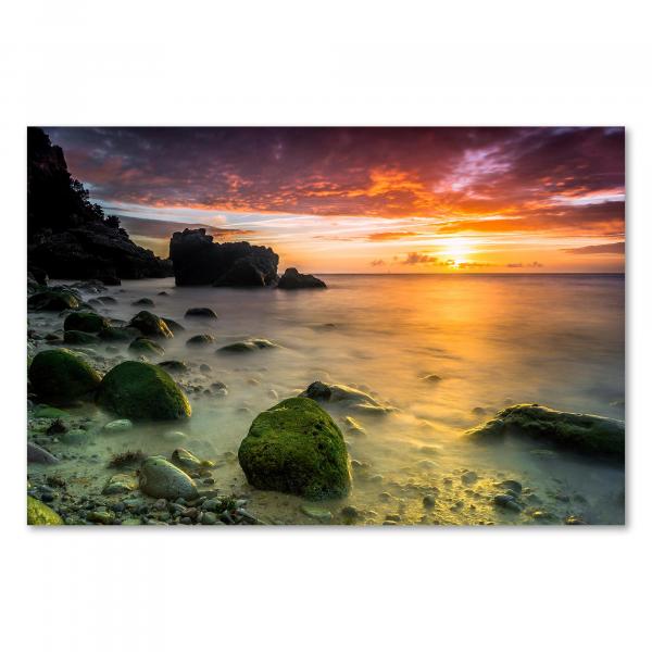 Grüne Felsen am Strand, im Hintergrund die untergehende Sonne und ein orangefarbener Himmel.