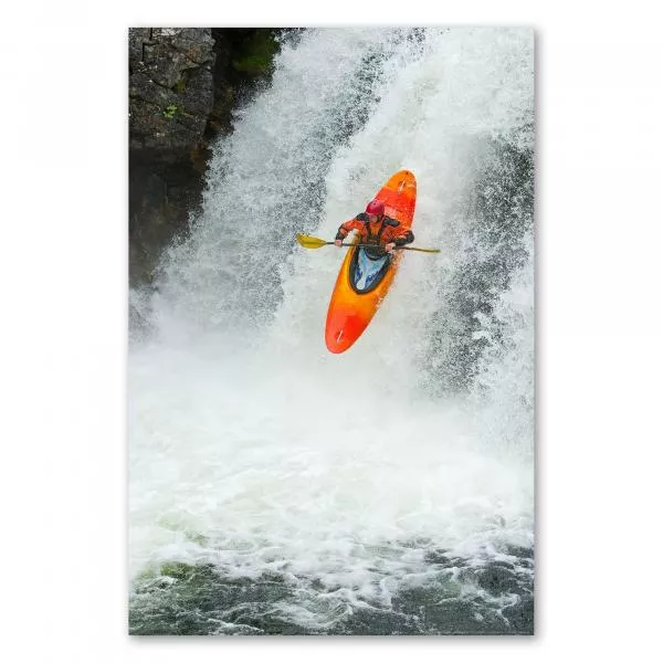 Ein Kajakfahrer stürzt sich in seinem knallorangen Kajak einen reißenden Wasserfall hinab und erlebt Abenteuer pur.