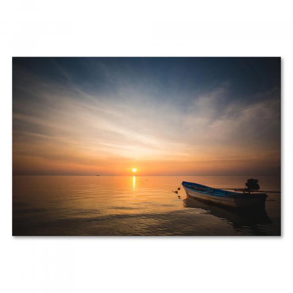 Stimmungsvolles Bild eines kleinen Bootes im Wasser vor dem Hintergrund eines farbenfrohen Sonnenuntergangs am Meer.