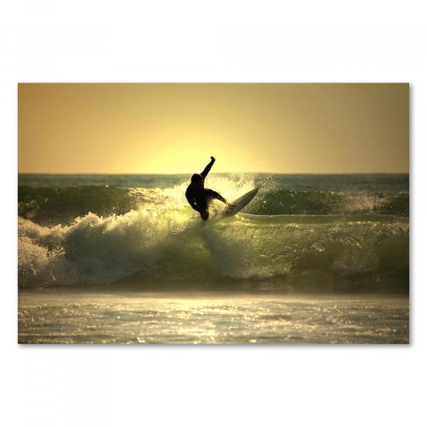 Silhouette eines Surfers, der eine Welle abreitet, während die untergehende Sonne die Szenerie golden färbt.