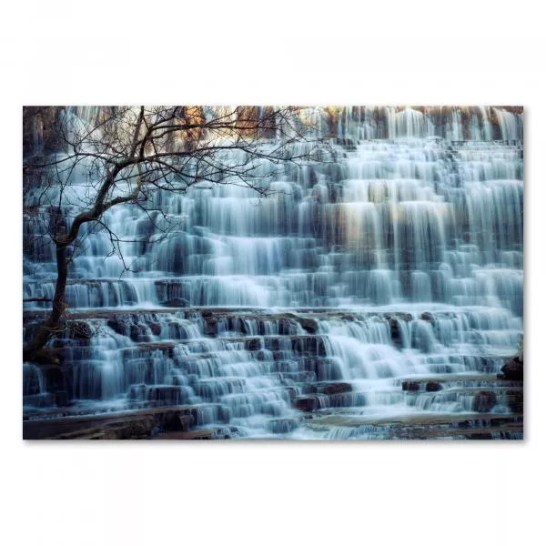 Mächtiger Wasserfall stürzt über Stufen, kahler Baum am Rand, unterstreicht Kraft der Natur.