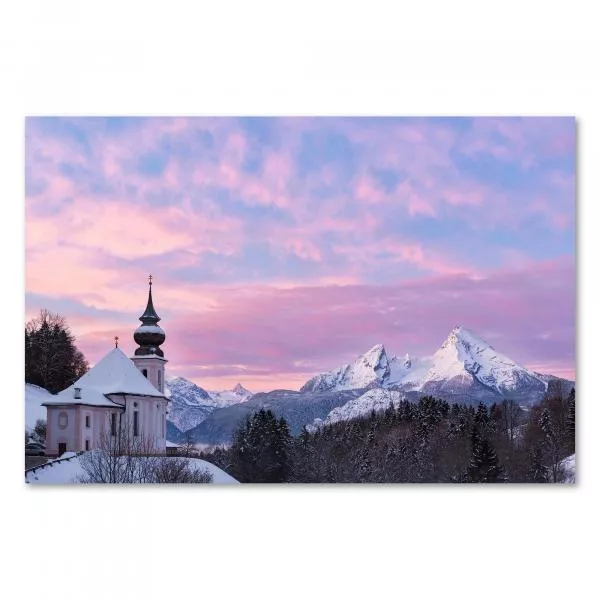 Eine schneebedeckte Kirche vor einer atemberaubenden Bergkulisse in den Alpen - ein Wintermärchen im Bild.