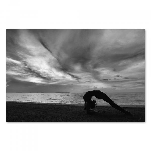 Schwarz-Weiß-Foto: Frau in Yoga-Kleidung, Brücke-Pose, Strand, Meer, bewölkter Himmel.